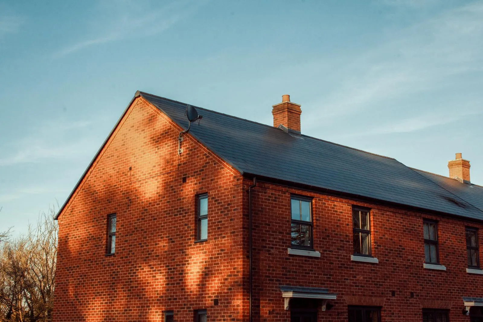 A red-brick new-build UK semi-detached home in late-afternoon sunlight — modern housing stock representative of the recent estate development around Great Shelford and the southern Cambridge fringe.