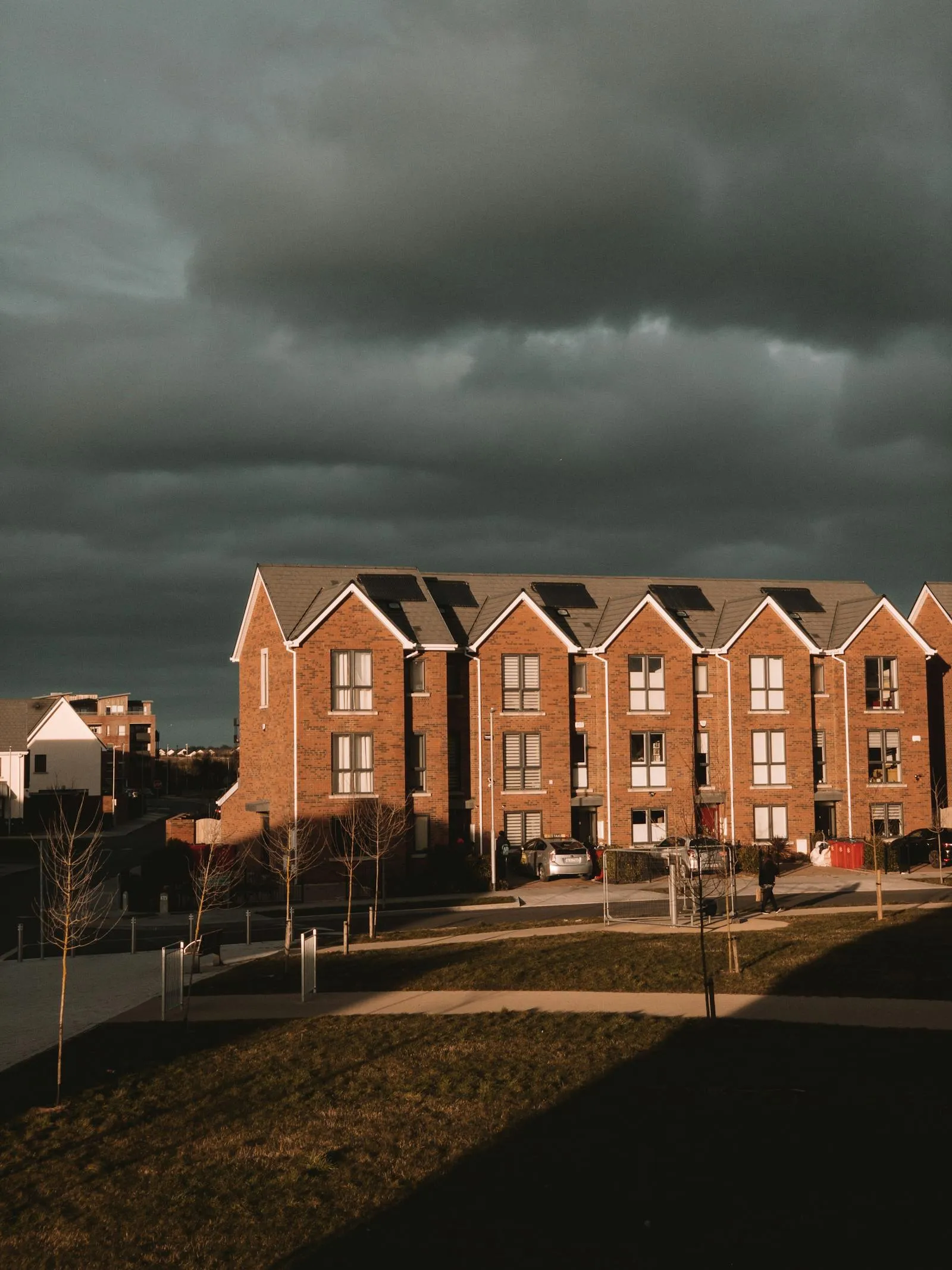 A terrace of new-build townhouses with rooftop solar PV panels against a dramatic UK sky — modern housing stock representative of recent development around the De Freville area.